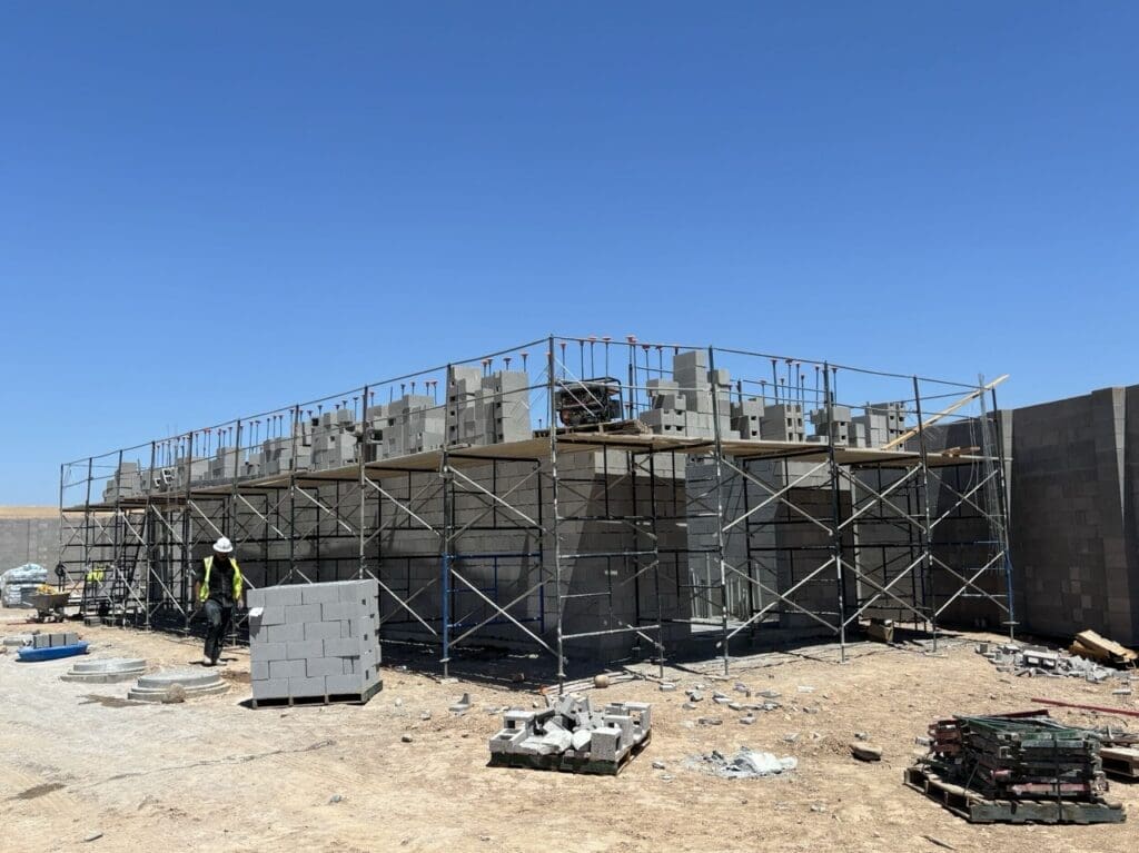 CMU wall construction in progress with elevated scaffold system, rebar dowels, and staged masonry units during structural build-out at City of Phoenix Booster Pump Station.