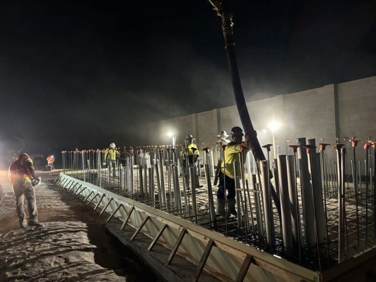 Nighttime concrete placement of reinforced slab using pump truck, with crews placing and consolidating concrete around dense vertical embeds and conduit sleeves at City of Phoenix Booster Pump Station