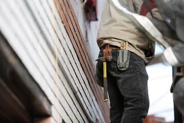 Construction worker with tool belt and hammer standing beside stacked building materials.