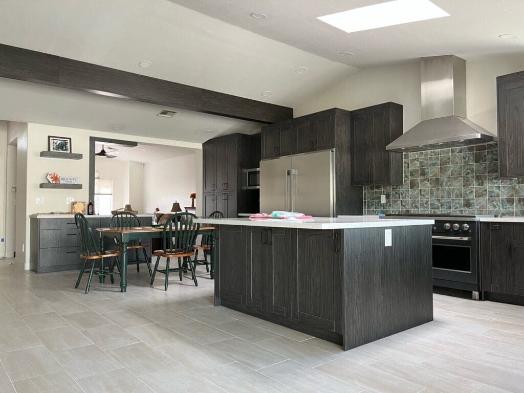 Finished Ahwatukee kitchen remodel showcasing a modern open-concept layout with custom dark cabinetry, waterfall-style quartz island, stainless steel range hood, skylight lighting, contemporary tile flooring, and upgraded dining integration for a clean luxury finish.