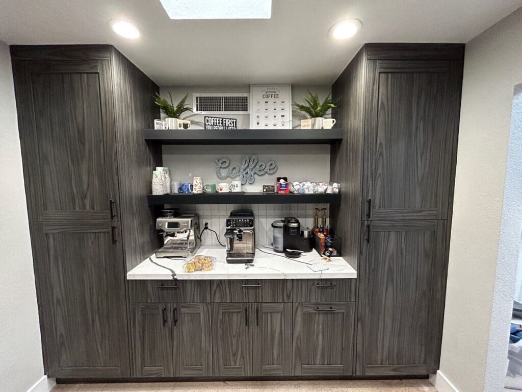 Built-in coffee station with dark wood cabinets, a marble countertop, and open shelves displaying mugs, coffee supplies, and small appliances including espresso and coffee machines.