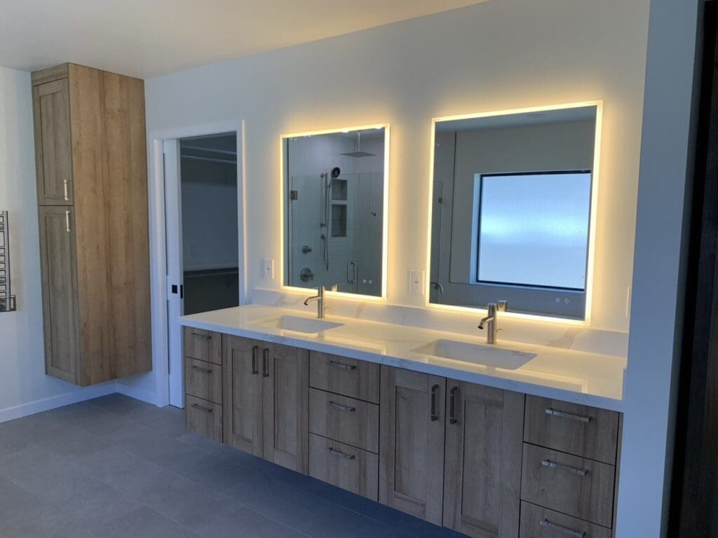 Modern double vanity with wood cabinetry, quartz countertop, and backlit mirrors, complemented by a clean, spa-style bathroom design.