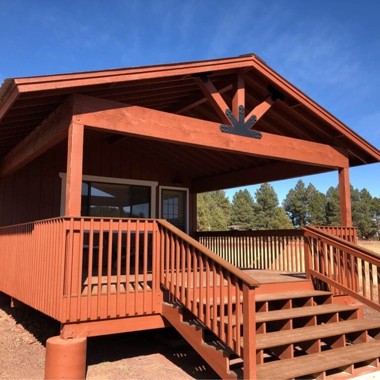 Front view of completed covered patio with exposed beams, new wood stairs, and railings under clear sky.