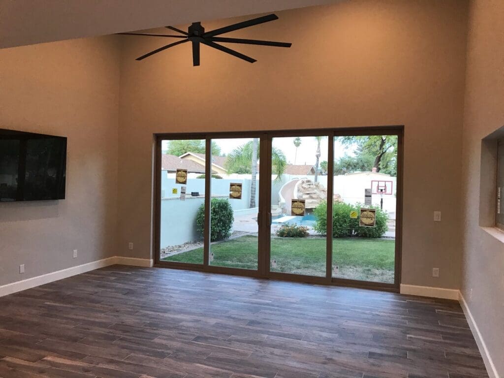 Modern casita living room with vaulted ceilings, large sliding glass doors, wood-look flooring, oversized ceiling fan, and seamless indoor-outdoor views to the backyard and pool area.