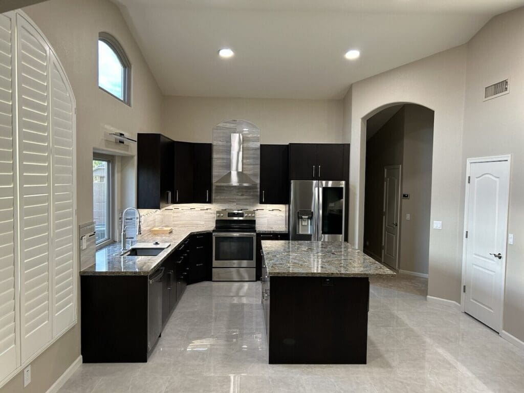 Phoenix kitchen remodel featuring open-concept layout, oversized granite island, stainless steel appliances, and dark modern cabinetry with vaulted ceilings