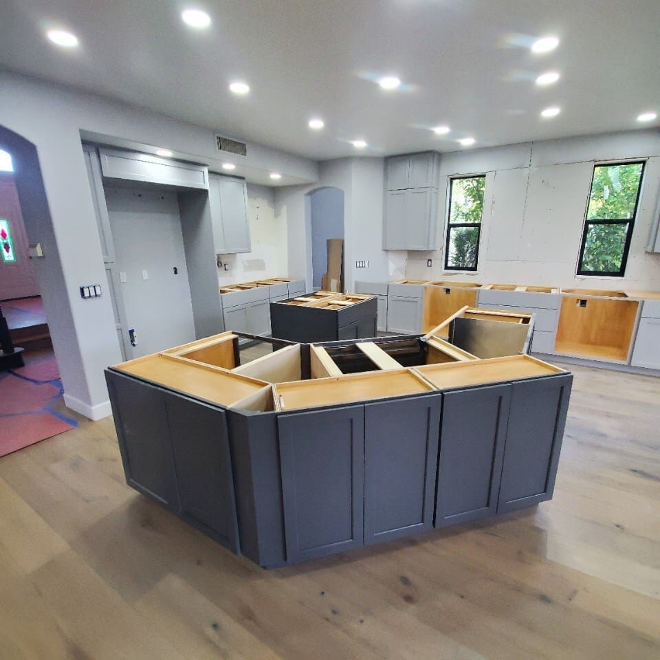 Modern kitchen remodel in progress during the Phoenix whole house renovation, showcasing custom gray cabinetry installation, oversized kitchen island framing, upgraded hardwood flooring, and recessed lighting throughout the space.