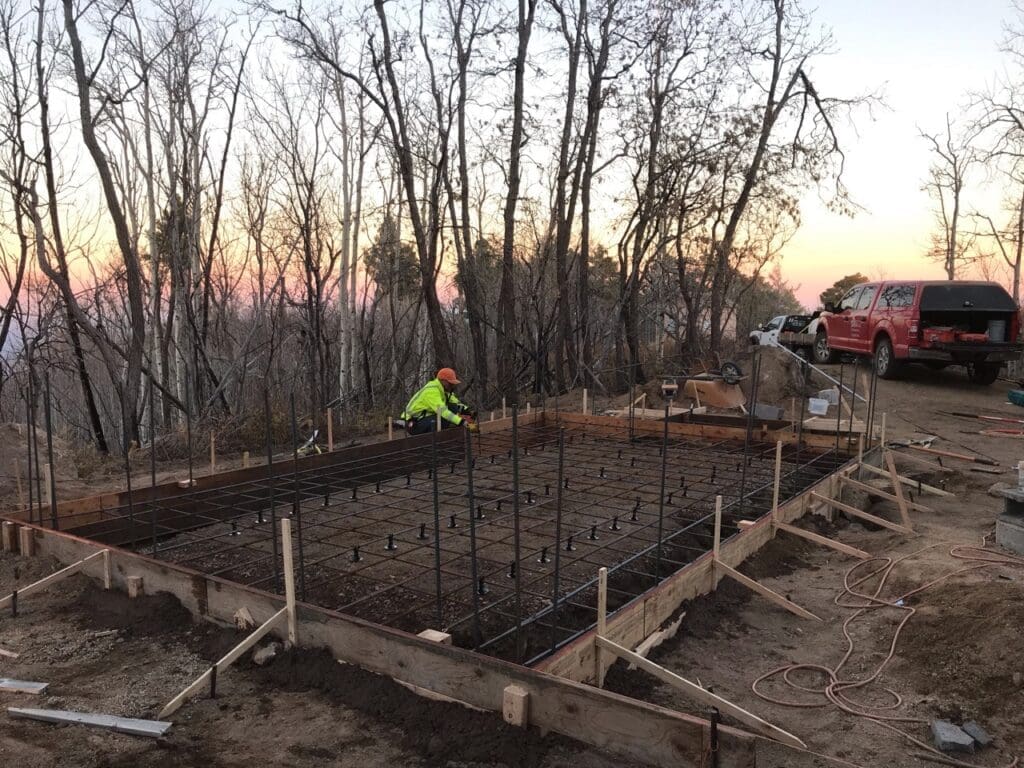 Construction worker preparing reinforced concrete slab formwork and rebar installation for the Pinal Peak equipment shelter foundation.