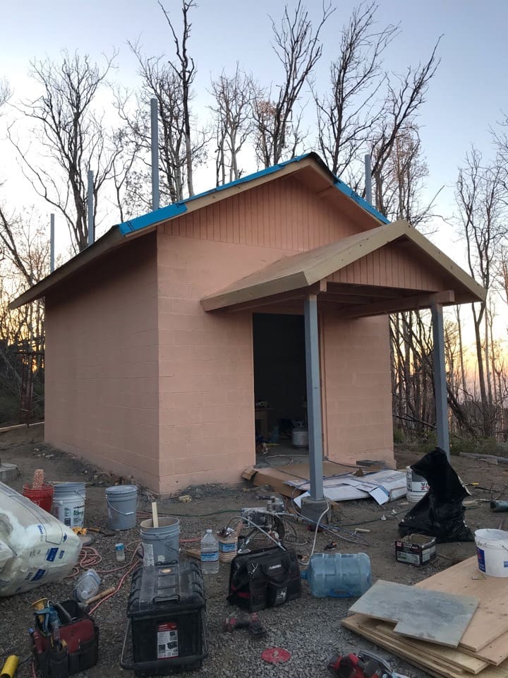 Front exterior view of the Pinal Peak equipment shelter during final construction stages, featuring completed masonry walls, covered entry canopy, and roof underlayment installation at the mountain communications site.