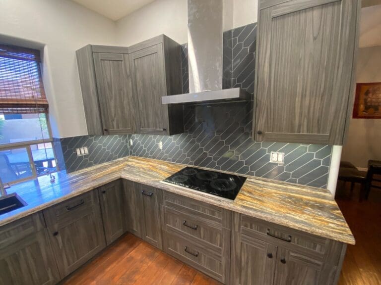 Modern cooking area featuring textured gray cabinetry, dramatic stone countertops, a sleek black geometric tile backsplash, and a stainless steel range hood for a bold contemporary finish.