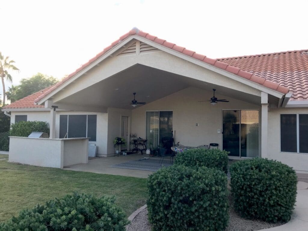 Completed Scottsdale patio renovation featuring a new gable roof with ceiling fans, fresh stucco finish, and an upgraded outdoor kitchen area overlooking a landscaped backyard