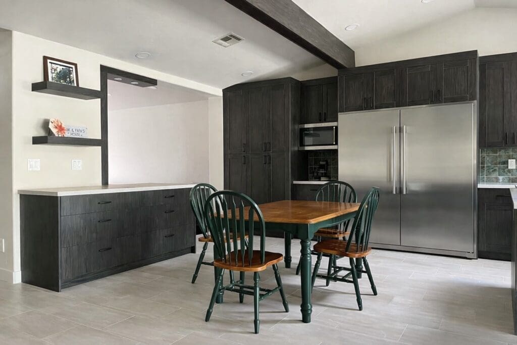 Modern kitchen and dining area with dark wood cabinets, a stainless steel refrigerator, a built-in microwave, and a wooden table surrounded by four green chairs on a tiled floor.